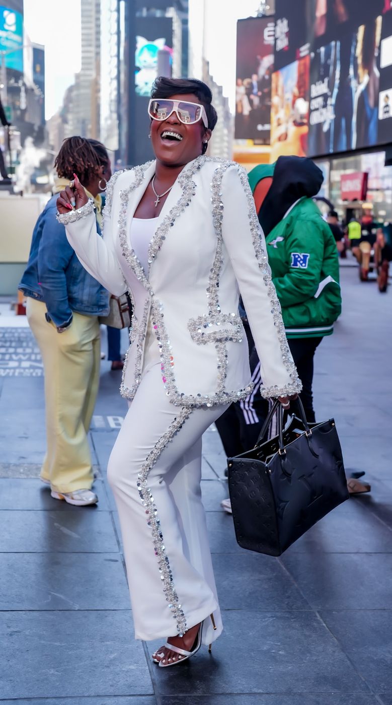 Jessica laughing in Times Square in a white embellished suit and College Gurl Sunnies